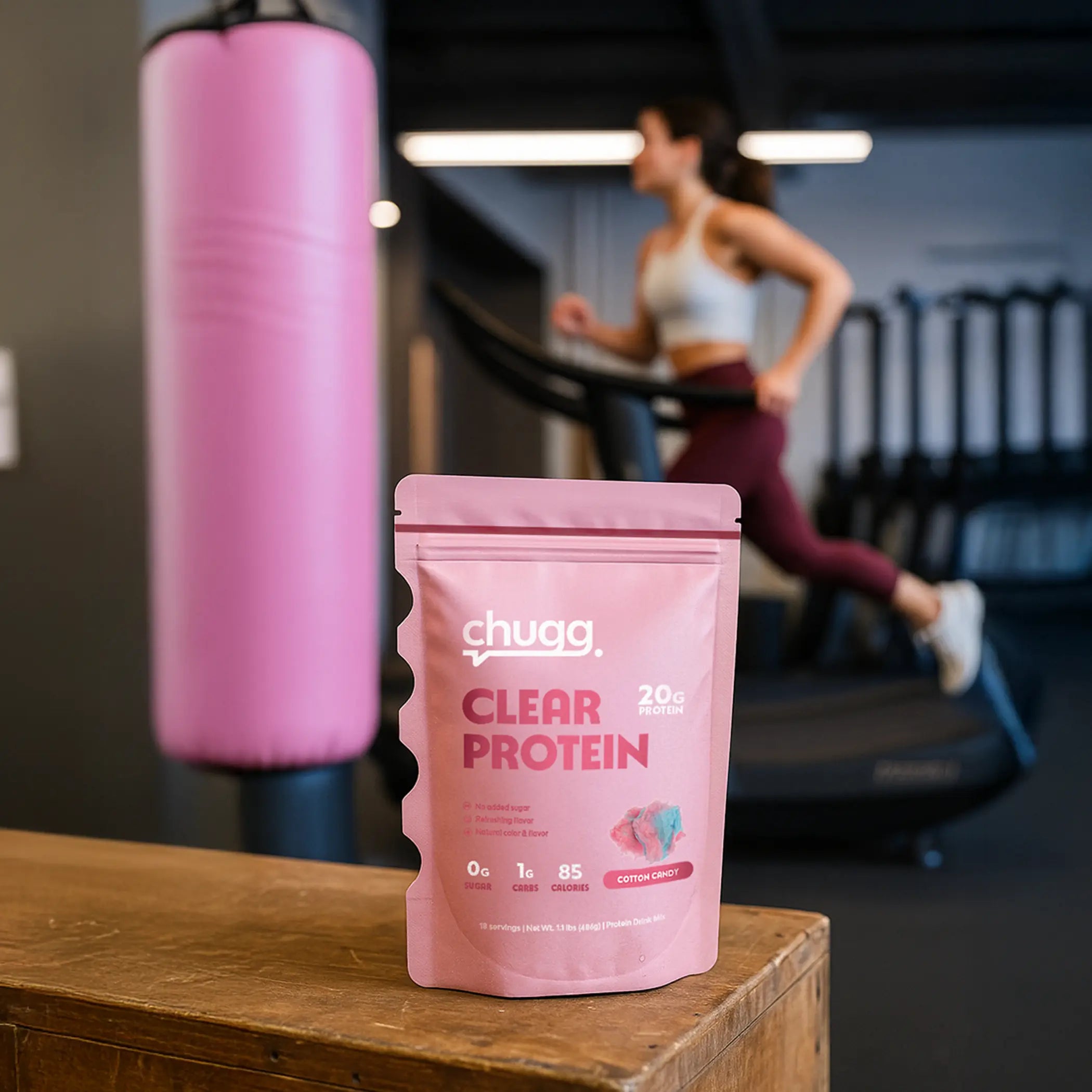 Chugg Clear Protein package on a wooden surface with a person exercising in the background.